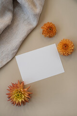 Blank paper card with mockup copy space, elegant flower buds, crumpled blanket on beige background. Top view, flat lay minimalist aesthetic brand template