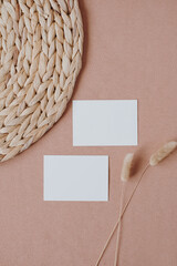 Blank paper card with mockup copy space, elegant dried rabbit tail grass stalk, straw rug on coral background. Top view, flat lay minimalist aesthetic bohemian brand template