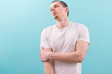 A tired man holds his arm and raises his head up on a blue background. Arms. Athletic....