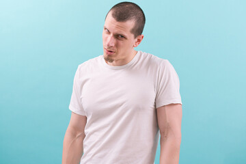 A model man in a white t-shirt suspiciously looks from under the forehead on blue background....