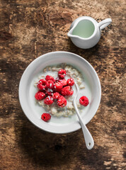 Vegetable milk oatmeal porridge with fresh raspberries on a wooden background, top view