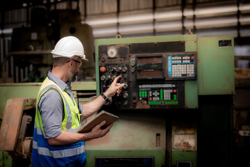 Caucasian male engineer or technician in safety uniform Working and checking machinery operation to maintenance information with online production data of the machinery in the tablet.