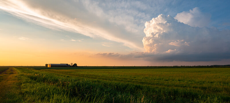 Idyllic image of a distant farm and storm cloud in the Dutch countryside during sunset