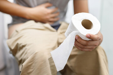 Man suffers from diarrhea hand hold tissue paper roll in front of toilet bowl. constipation in...