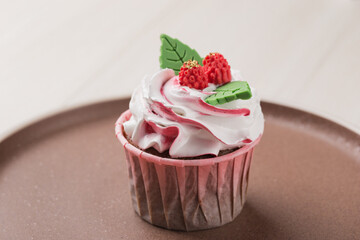 Homemade cupcake decorated with cream and figure chocolate on ceramic plate close up.
