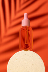 Cosmetic bottle with serum or oil on podium. Orange background with daylight and palm shadow. Sun protection lotion, sunscreen. Summer skin care concept with spf.