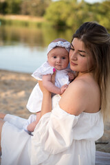 Fototapeta premium mom with a newborn baby sits on the beach, on the sand. mom holds a newborn baby in her arms.