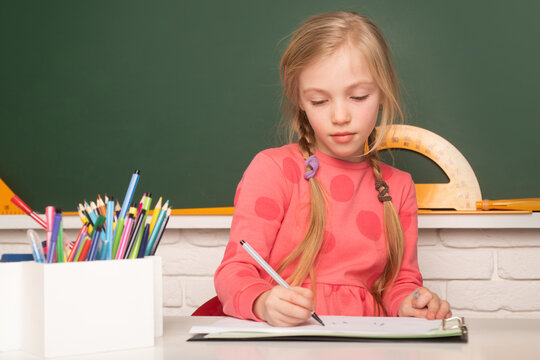 School student taking notes from book for study. School child near chalkboard in school classroom. - Powered by Adobe