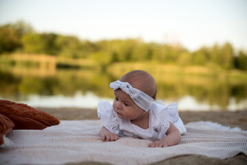 a newborn child lies on a blanket, on the shore. flowers lie nearby.