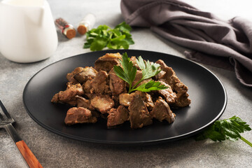 Fried or baked chicken liver with onion and sauce, green parsley leaves on a plate. Meat dish...