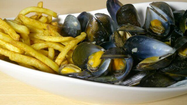 Closeup dolly shot of moules frites &ndash; cooked mussels in their shells with fries &ndash; in a long bowl, ready to eat.