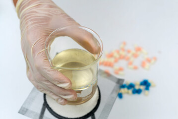 The biologist heats up the liquid for the study, there are pills on the table. High quality photo