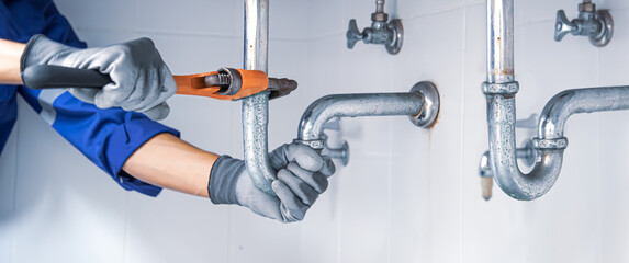 Technician plumber using a wrench to repair a water pipe under the sink. Concept of maintenance,...