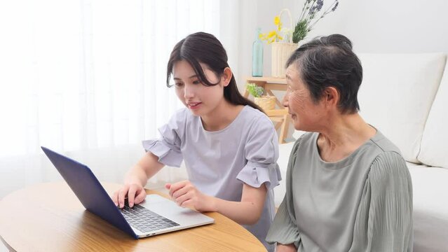 リビングでノートパソコンの前で会話する孫と祖母