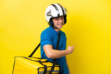 Young Brazilian man with thermal backpack isolated on yellow background pointing back