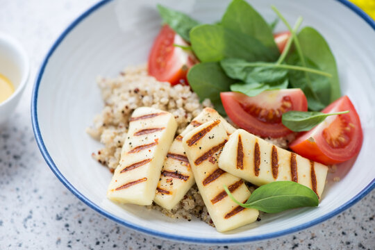 Close-up of quinoa, grilled halloumi cheese, spinach and tomato salad served in a white plate, selective focus
