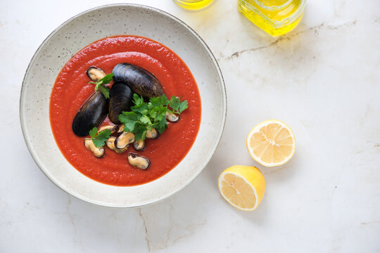 Plate of tomato cream-soup with mussels on a beige marble background, horizontal shot with copy space, top view
