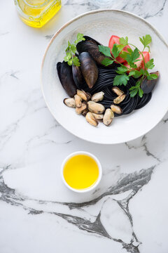 Plate of squid-ink spaghetti with mussels and fresh parsley, flat lay on a black and white marble background, vertical shot with space