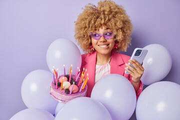 Happy woman with curly hair wears trendy sunglasses and formal pink jacket celebrates birthday...