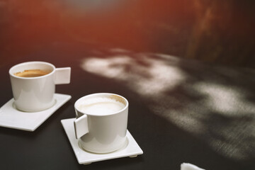 Two cups of cappuccino with latte art on dark background. Beautiful foam, greenery ceramic cups, stylish toning, place for text.