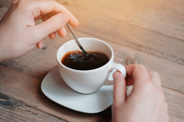 Close up of man enjoying in cup of morning coffee and mixing it with a spoon.