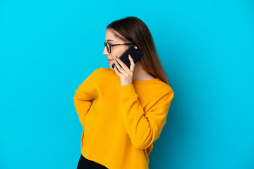 Young caucasian woman isolated on blue background keeping a conversation with the mobile phone with someone