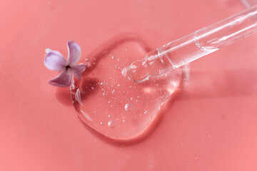 Closeup of pipette with serum, oil, gel with lilac flowers on pink background. Skin care, natural beauty products presentation concept. Macro. Romantic floral composition. Front view, high angle shot