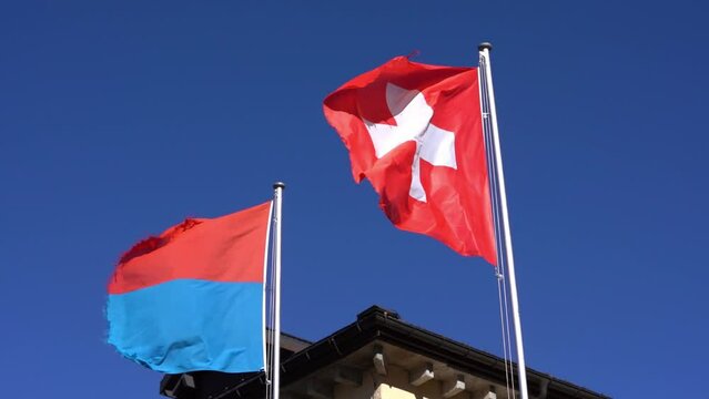 Swiss flag and flag of Canton Ticino blowing in the wind at St. Gotthard Pass in the Swiss Alps on a sunny summer day. Slow motion movie shot June 25th, 2022, Gotthard Pass, Switzerland.