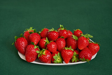 white plate filled with red strawberries on a green background