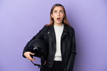 Young caucasian woman holding a motorcycle helmet isolated on purple background looking up and with surprised expression