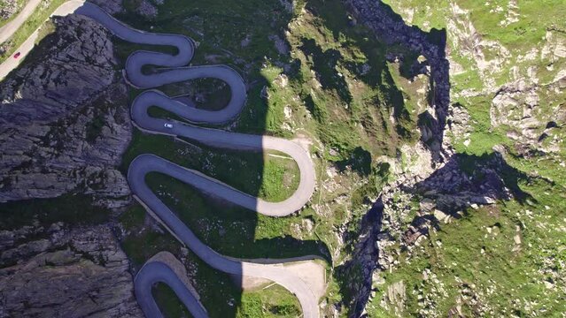 Aerial view of Tremola pass road with white car going down at Gotthard Pass on a sunny summer day. Movie shot June 25th, 2022, Gotthard Pass, Canton Ticino, Switzerland.