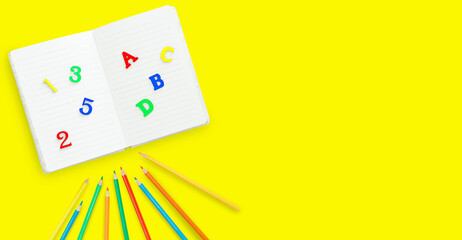 School notebook, colourful bright letters and numbers, colourful pencils on yellow background with copy space flat lay. Concept back to school.