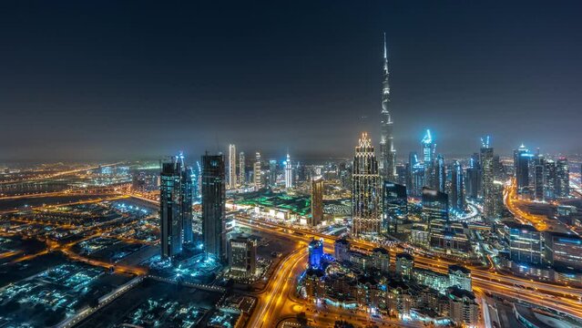 Aerial panorama of tallest towers in Dubai Downtown skyline and highway in creek district night timelapse. Financial district and business area in smart urban city. Skyscraper and high-rise buildings