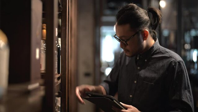 A male bartender is using a tablet to check product in a store.
