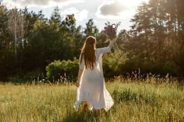Fototapeta na wymiar Young beautiful woman, wearing white dress, holding flowers and dancing on the meadow. Girl joying nature and freedom. Natural beauty. Dance, movement. Mental health, stress free, dreaming. Sunset.