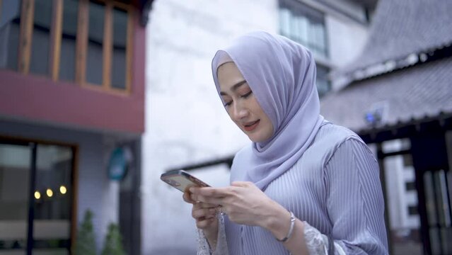 Portrait of muslim woman user businesswoman in pink hijab on street holding mobile phone using smartphone for chatting browsing typing message smiling shopping online app