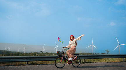 Young muslim woman electric green bike bicycle by windmill farm, windmills isolated on a beautiful...