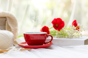 Coffee morning.  Red steaming cup of hot coffee for relax after working hobbies crochet on white wooden near window with flowers.
