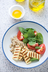 Plate with quinoa, halloumi cheese, spinach and tomato salad, vertical shot on a beige granite background, elevated view