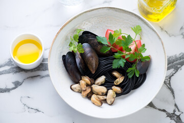 Plate of mussels with black spaghetti, tomatoes and parsley on a black and white marble background, horizontal shot