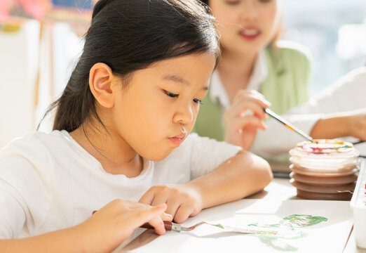 cute little children think, wear white shirt, look at paper, painting color on paper art in education classroom. asian beautiful children happy and fun color painting education in small school