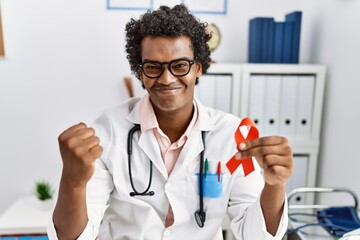 African doctor man holding support red ribbon celebrating victory with happy smile and winner...