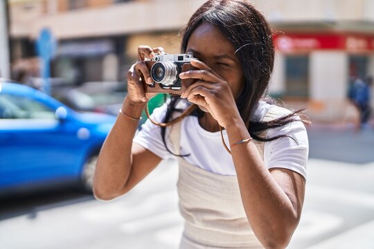 Young african american woman smiling confident using vintage camera at street