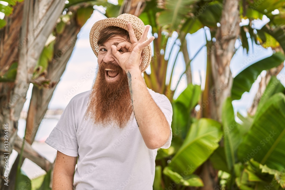 Sticker Caucasian man with long beard outdoors on a sunny day wearing summer hat smiling happy doing ok sign with hand on eye looking through fingers