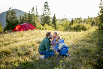 Naklejka na ściany i meble Portrait of a lovely couple with little girl hug together while travel in the mountains. Young caucasian family spend summer time on nature
