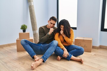 Obraz premium Young couple sitting on the floor at new home feeling unwell and coughing as symptom for cold or bronchitis. health care concept.