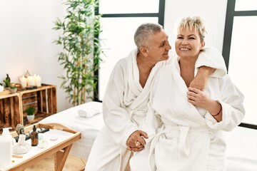 Fototapeta premium Senior caucasian couple smiling happy and hugging sitting on massage table at beauty center.