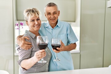 Senior caucasian couple smiling happy drinking wine at the kitchen.