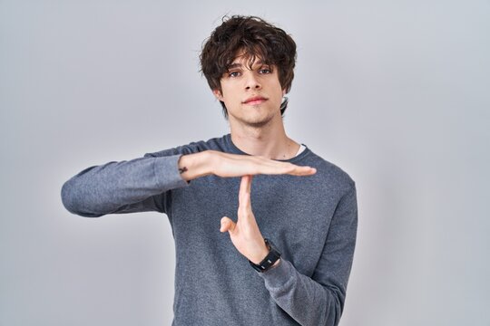 Young man standing over isolated background doing time out gesture with hands, frustrated and serious face