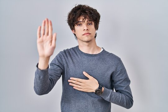 Young man standing over isolated background swearing with hand on chest and open palm, making a loyalty promise oath